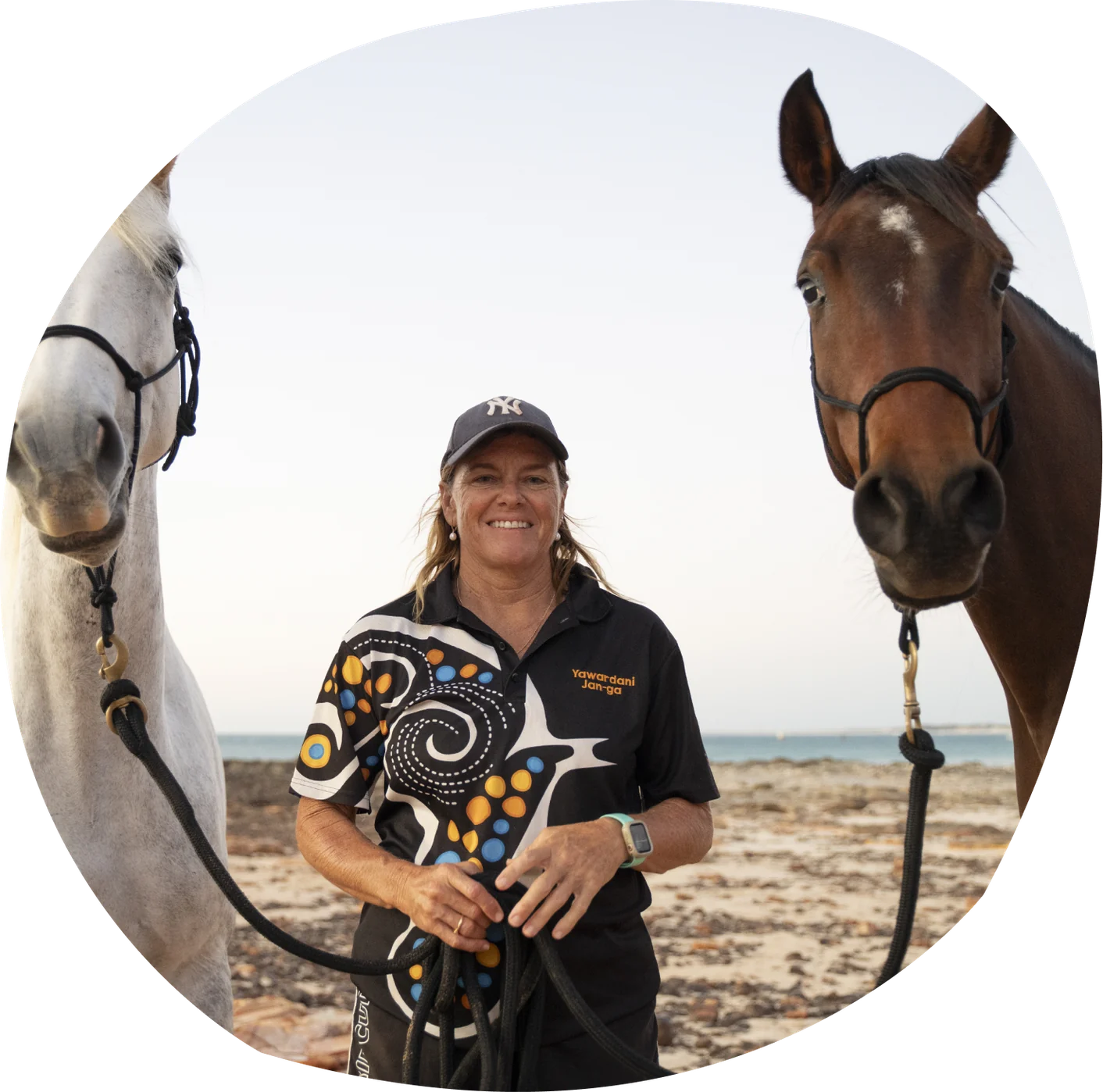 Professor Juli Coffin smiling on a beach beside a brown horse.