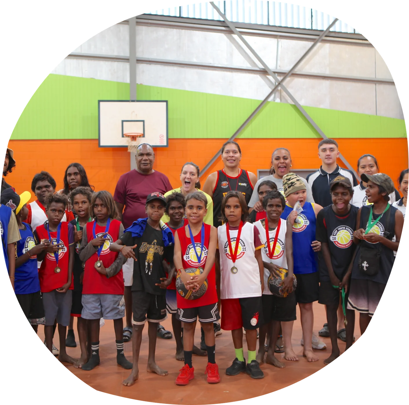 A large group of young people and adults in basketball uniforms and medals posing together in a sports hall.