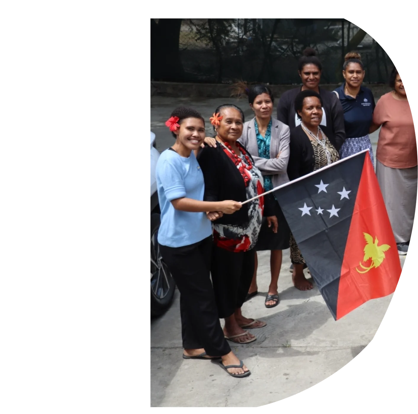 A group of women standing together outdoors, one holding the Papua New Guinea flag.